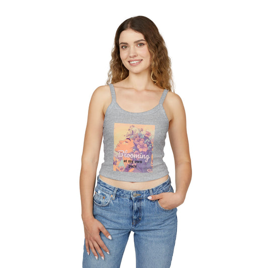 "Woman wearing a grey crop tank top with a colorful floral design and the phrase 'Blooming at my own pace,' paired with blue jeans, smiling with hand in pocket."