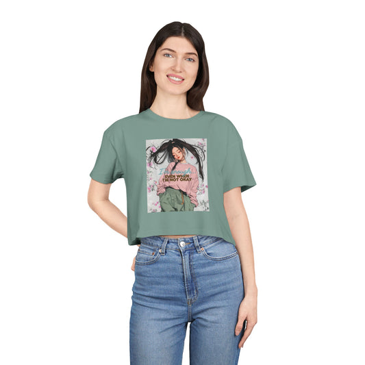 A woman wearing a green crop tee with a floral design and text that says 'I AM ENOUGH'. The tee has short sleeves and a round neckline.